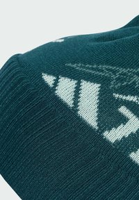 Prim-plan al unui material tricotat de culoare verde închis, cu un model geometric alb și o textură ribonată pe margine.