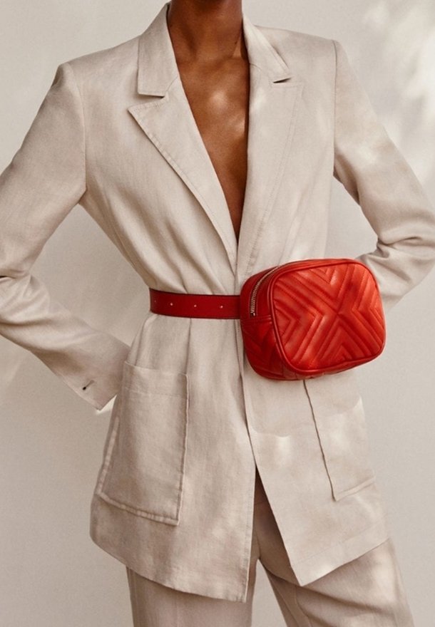 Blazer en lin beige avec un décolleté en V profond, associé à un sac ceinture matelassé rouge. Le sac présente un motif géométrique et un design élégant.