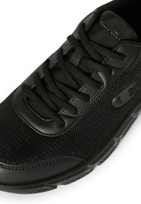 Zapatilla deportiva negra con parte superior de malla y superposiciones sintéticas, puntera redonda, cierre con cordones y detalles texturizados en los laterales.