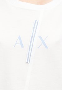 Λευκό πουκάμισο με φωτεινό μπλε λογότυπο "A | X" που καλύπτεται εν μέρει από έναν κάθετο λευκό λωρίδα με τρεις φωτεινό μπλε ρίγες.