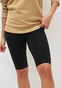 Shorts de vélo en coton mélangé noir avec une coupe extensible, longueur mi-cuisse et texture lisse, associés à un sweatshirt beige neutre.