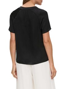 Zwarte blouse met korte mouwen en een zachte textuur, met een ronde halslijn en geplooide rugdetails. Draagt bij lichte gekleurde broeken.