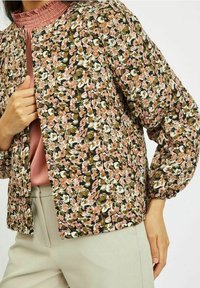 Blommig bomberjacka med en mörkgrön bakgrund, prydd med rosa och vita blommor, puffärmar och en enkel tryckknappsstängning.