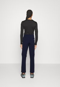 Tumesinised püksid, millel on slim fit sobivus ja elastsest kangast, tagakotis oleva taskuga ning siledat tekstuuri, mida täiustab must pikkade varrukatega pluus ja hallid kingad.
