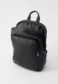 Sac à dos en cuir noir avec une surface texturée, fermetures zippées doubles, poche avant et détail de logo. L'intérieur présente une doublure à motif.