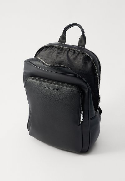 Sac à dos en cuir noir avec une surface texturée, fermetures zippées doubles, poche avant et détail de logo. L'intérieur présente une doublure à motif.