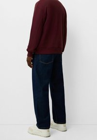 Sudadera burdeos con cuello redondo, puños acanalados, combinada con vaqueros de corte ancho azul oscuro y zapatillas blancas. Diseño sencillo, sin logotipos visibles.