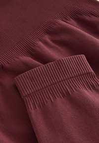 Indumento bordeaux con texture a costine e una finitura liscia. Presenta un polsino aderente e modelli a costine variabili su tutto il tessuto.