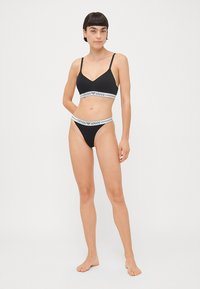 Black lingerie set featuring a bralette with thin straps and a thong. Both pieces have a white branded waistband with "Emporio Armani."