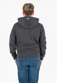 Felpa grigia con cappuccio e superficie liscia, dotata di polsini e orlo a costine. Indossata con jeans in denim blu, girata di spalle rispetto alla fotocamera.