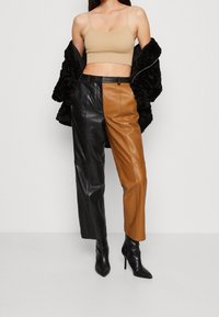 Svarta och bruna läderbyxor med blockfärger, tillsammans med en beige, kort tanktop och ett svart, strukturerat ytterplagg. Svarta klackar fulländar looken.