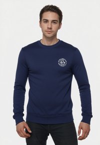 Sudadera azul marino de manga larga y cuello redondo. Presenta un gráfico blanco en el pecho y puños y dobladillo acanalados. Textura de tela suave.