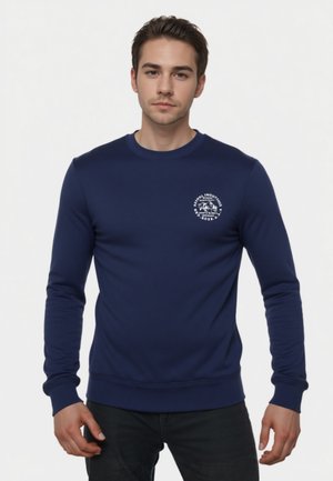 Felpa blu navy con maniche lunghe e collo rotondo. Presenta una grafica bianca sul petto e polsini e orlo a coste. Tessuto dalla texture liscia.