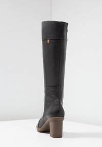 Black leather knee-high boot with a rounded toe and stacked heel. Features a folded cuff and a tan accent label near the top. Smooth texture.