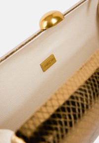 Gold metallic handbag interior featuring a cream fabric lining, a gold tag with "Marc Cain," and a textured mesh detail.
