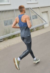 Vêtements de course : un débardeur sans manches, bleu marine et gris, associé à un legging noir avec du texte. Les chaussures sont vertes avec des accents jaunes.