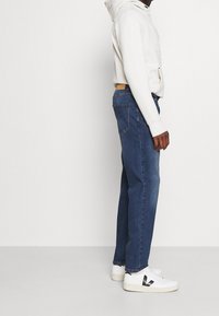 Dark blue straight-leg jeans with a classic fit, paired with a white hoodie and white sneakers featuring black accents.