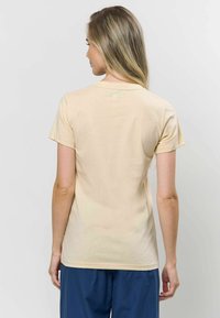 Világos bézs színű, rövid ujjú pamut póló, kerek nyakkivágással és sima textúrával. Diszkrét varrás részlet található a hátsó részen.