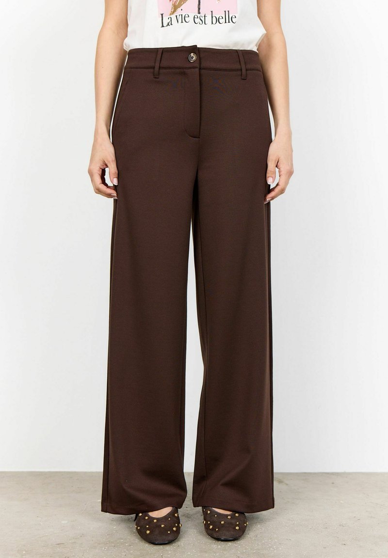 Pantalones de pierna ancha marrones, hechos de una tela suave, con cierre de botón delantero y bolsillos laterales. Combinados con zapatos planos oscuros adornados.