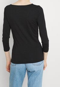Top nero a maniche lunghe con scollatura ampia, realizzato in materiale morbido, abbinato a jeans in denim blu chiaro. Texture liscia, design minimale.