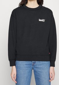 Sweatshirt noir en mélange de coton, doté d'un col rond, d'épaules tombantes, et d'un petit logo blanc Levi's sur la poitrine.