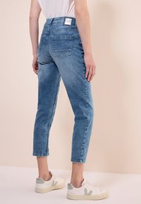 Ljust blå denimjeans med hög midja, kort längd och två bakfickor. Matchat med vita sneakers med gröna detaljer.