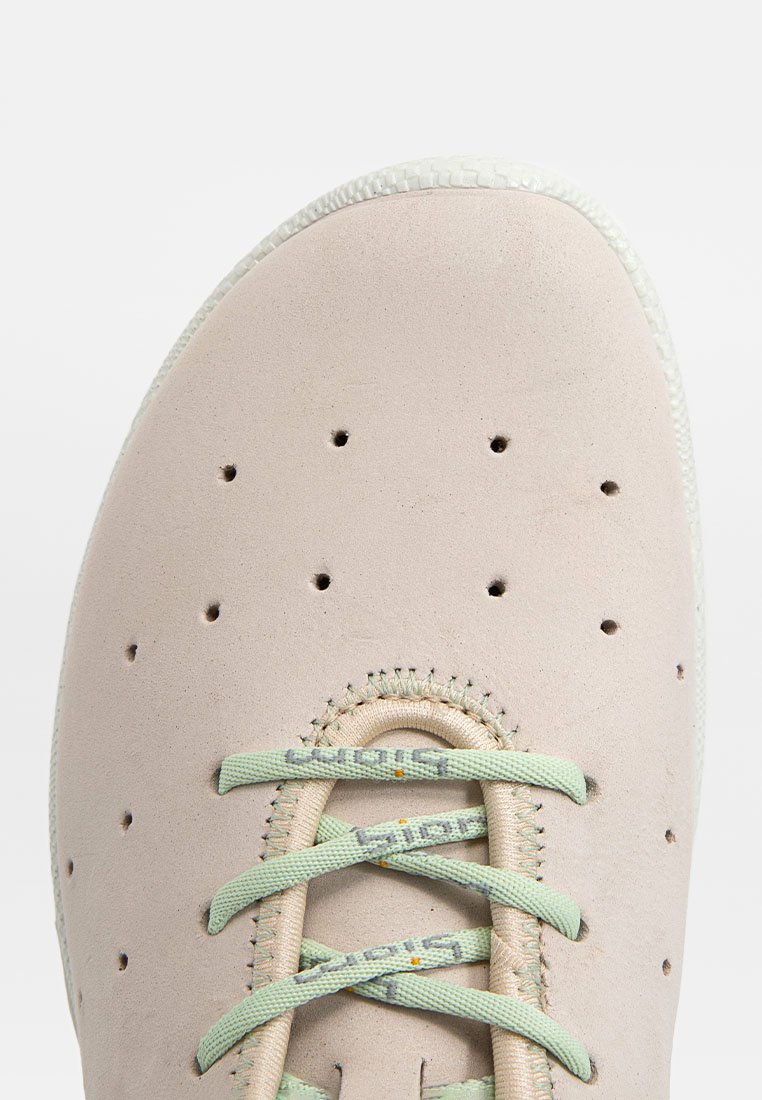 Jasnoróżowe sneakersy z teksturowaną cholewką z zamszu, perforacjami zapewniającymi wentylację oraz jasną zieloną sznurówką przewleczoną przez otwór na sznurówki.