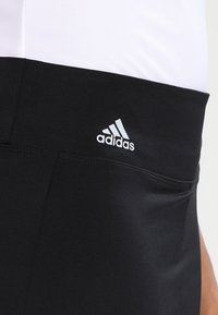 Pantalones cortos deportivos negros con una cinturilla elástica, que presentan un pequeño logo blanco de Adidas en el lado izquierdo y una textura de tela suave y elástica.