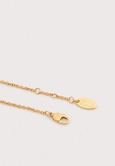 Κούμπωμα κολιέ αλυσίδας από χρυσό με οβάλ ταμπελάκι χαραγμένο με την επιγραφή «Vivienne Westwood» σε λευκό φόντο.