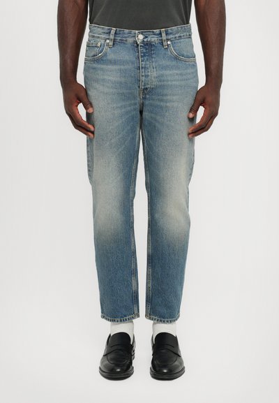 Jean en denim bleu clair avec une coupe droite, une apparence délavée et un design à cinq poches. Porté avec des mocassins noirs et des chaussettes blanches.