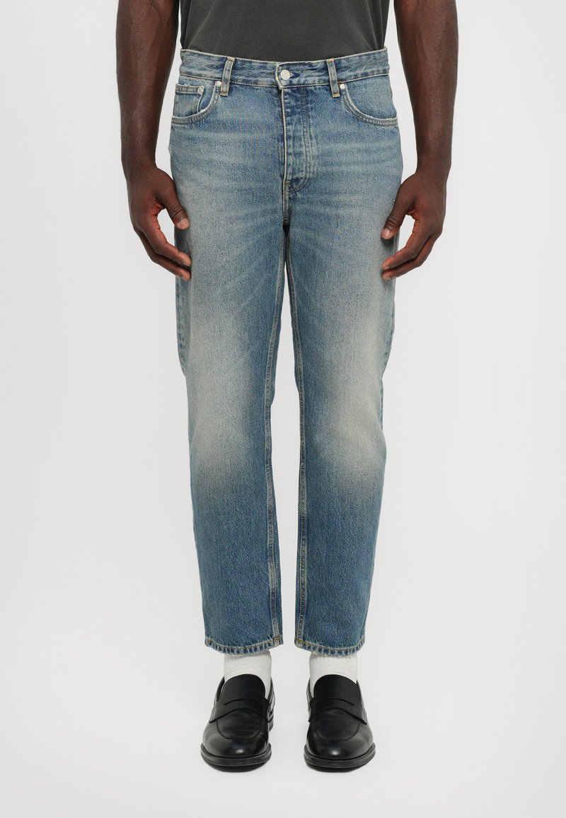 Light blue denim jeans with a straight fit, faded appearance, and five-pocket design. Worn with black loafers and white socks.