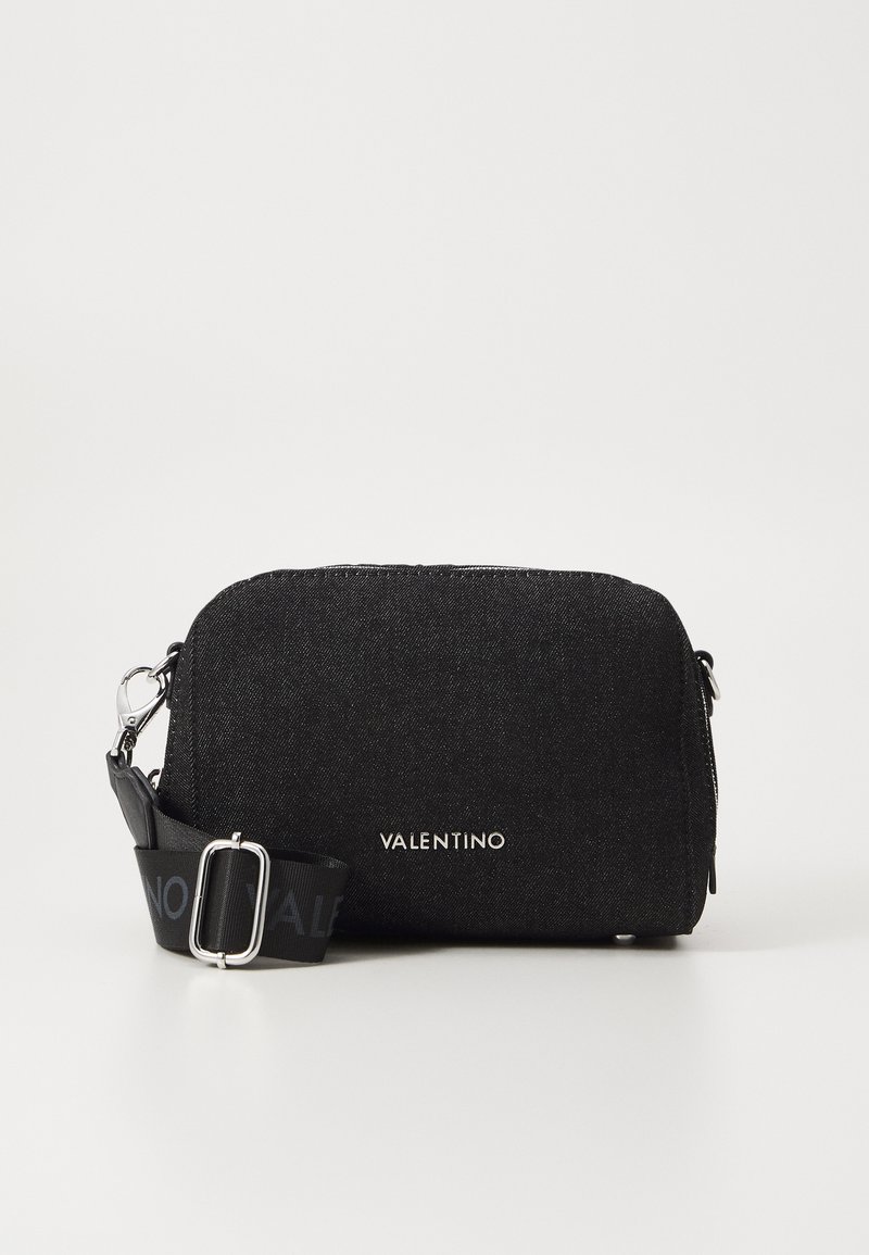 Sac bandoulière noir en tissu avec fermeture éclair, doté d'une sangle imprimée du logo et d'accents en métal argenté. Texture lisse et forme arrondie.
