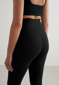 Svarta högmidjade leggings med en slät textur, med sömdetaljer baktill och en kroppsnära design.