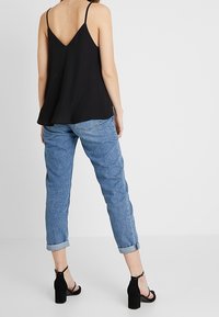 Svart ärmlös topp med V-format rygg, kombinerad med avslappnade blå jeans som är uppvikta vid fållen, och svarta blockklack-sandaler med ankelsnörning.