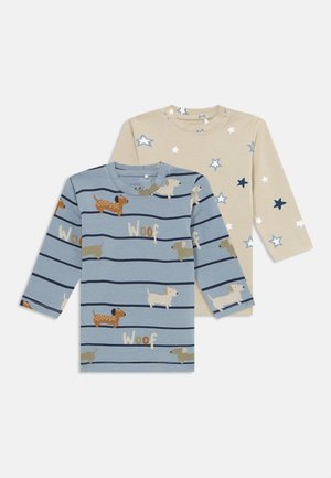 Twee kindermouwen shirts met lange mouwen: een beige met blauwe en witte sterren, en een blauwe met hondenillustraties, strepen en de tekst "Woef".