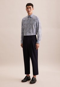 Blauw paisley-gepatroond shirt, cropped ontwerp, lange mouwen. Gecombineerd met hoge zwarte broeken en zwarte veterschoenen.