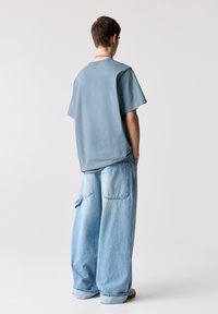 Løs pasform blå t-shirt med en blød tekstur, parret med baggy lysblå jeans med to store baglommer. Minimalistisk design.
