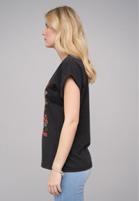 Musta lyhythihainen t-paita, jossa on käännetyt hihat ja edessä graafinen printti. Yhdistetty vaaleansinisiin slim-fit-farkkuihin.