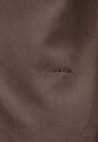 Καφέ ύφασμα με διακριτικό κεντημένο λογότυπο «Calvin Klein» σε νήμα που ταιριάζει στη μέση δεξιά πλευρά.