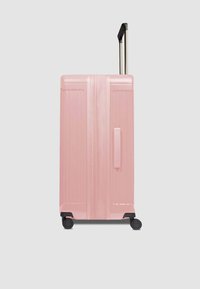Valigia rigida rosa con texture a coste verticali, manico retrattile, due ruote nere e maniglia laterale per un facile trasporto.