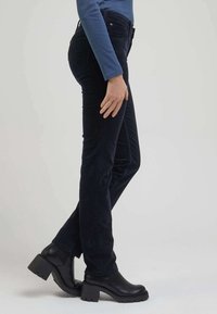 Jeans de mezclilla negra con un corte slim, con una cintura de altura media y costuras sutiles en los bolsillos. Combinados con botas negras de tacón grueso.