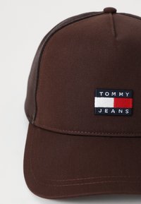 Smešani naočale od teksturirane tkanine s logotipom "TOMMY JEANS" u bijeloj i plavoj boji, naglašeni crvenom i bijelom prugom.