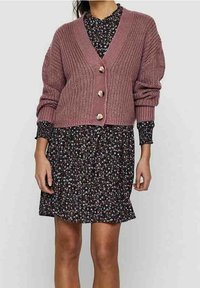 Virkat rosafärgad cardigan med V-hals och fyra knappar, lager på lager över en svart blommig klänning med lång ärm.