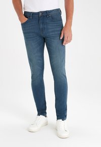 Dunkelblaue Slim-Fit-Jeans aus Denim, mit klassischem Fünf-Taschen-Design und subtilen Farbabstufungen. Kombiniert mit weißen Sneakers.