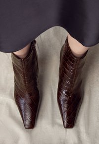 Braune Leder-Stiefeletten mit Krokodilmuster, spitzer Schuhspitze und Reißverschluss. Glatte Textur und strukturiertes Design.