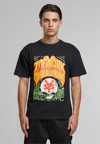 Sort bomulds t-shirt med et livligt grafisk print i orange, grønne og hvide farver, der viser tekst og et kraniumdesign. Korte ærmer.