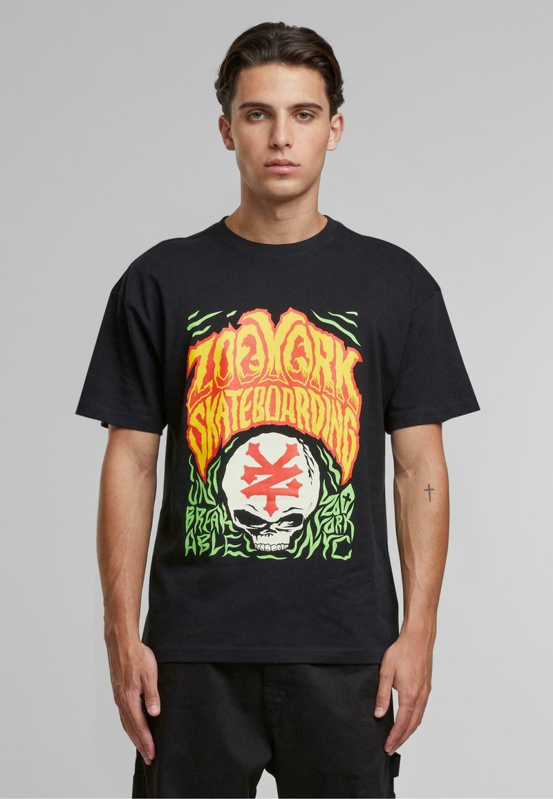 Sort bomulds t-shirt med et livligt grafisk print i orange, grønne og hvide farver, der viser tekst og et kraniumdesign. Korte ærmer.