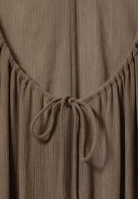 Tissu côtelé marron avec un col rond, doté de détails froncés et d'un accent noué à l'arrière. Texture douce, design simple.
