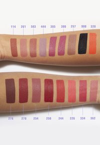 Läppstiftsprovningar på armar: 15 nyanser som sträcker sig från dämpade rosa till djupa röda, med matta och blanka finishar; alla märkta med nummer ovanför varje prov.