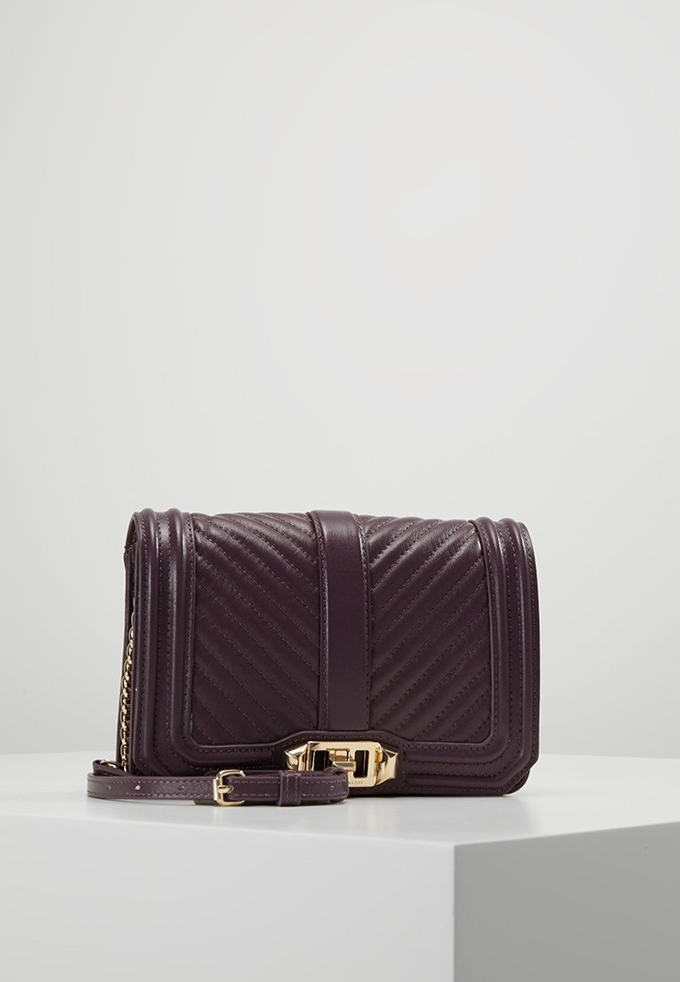 Borsa a tracolla in pelle viola con motivo a zigzag, hardware dorato e tracolla removibile. Forma rettangolare compatta, cuciture dettagliate.